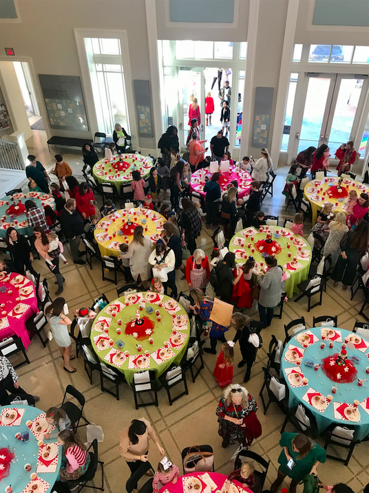 Many tables and chairs. Large crowd of people.